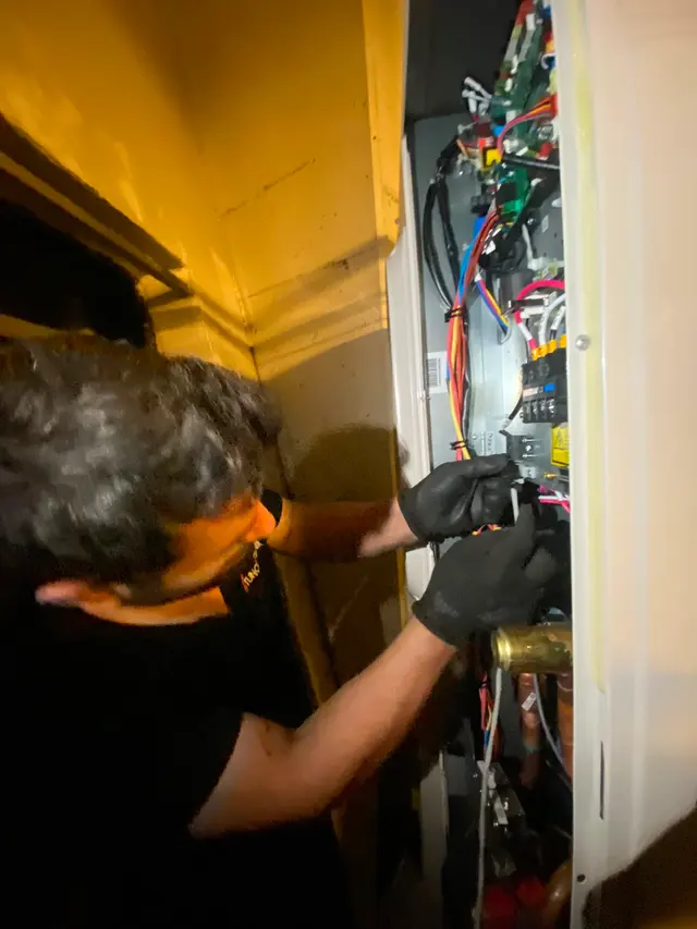 Tezgâhta açılmış bir kombi elektronik kartı; teknisyen lehim ve ölçüm yapıyor